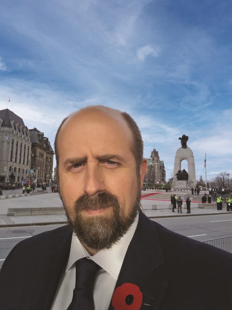 Un homme en costume et cravate debout devant le Musée canadien de la guerre à Ottawa.