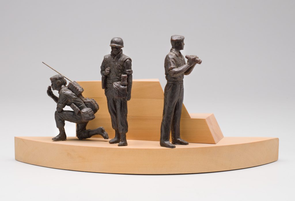 Une sculpture en bronze de trois hommes sur un socle en bois située au Musée canadien de la guerre à Ottawa.