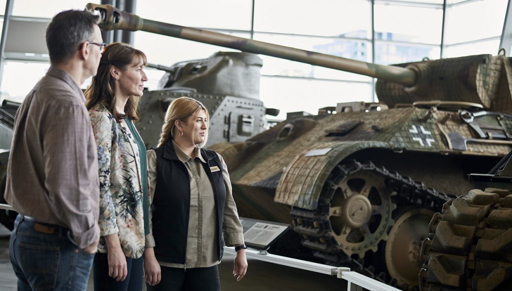 Trois personnes regardant un char dans un musée.